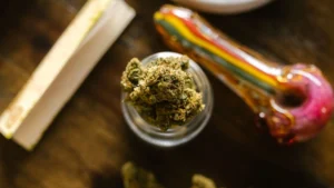 Close-up of small, whole-flower cannabis buds in a glass jar alongside a glass pipe and rolled joint, demonstrating low-dose options for daytime focus.